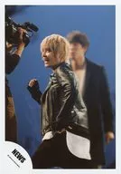 NEWS / Yuya Tegoshi / Above-the-knee ・ Costume black ・ Left facing ・ Mouth opening ・ Right hand fist ・ Cameraman ・ Members behind ・ Background blue / PV photography of "ヒカリノシズク" / Official Official photo