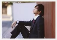 山田詹姆斯武/橫型·全身(足見斷)·坐著·服裝黑·白·領帶紅·製服·左手搭膝·身體向左·靠在牆上·背景白·茶色/電影先行上映活動會場限定銷售生寫真